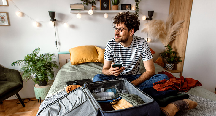 Jeune étudiant préparant sa valise en pensant à son budget voyage