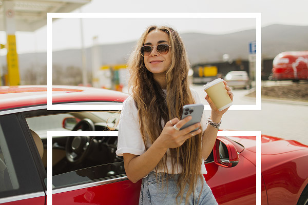 Jeune conducteur tenant un café et un smartphone à côté de sa voiture rouge