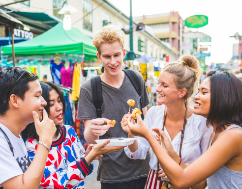Jeunes voyageurs dégustant des spécialités locales dans un marché à l’étranger